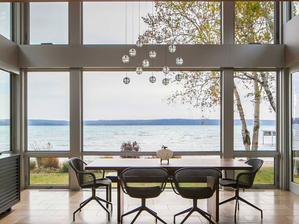 A dining area with large windows providing a scenic view of a lake and surrounding nature.