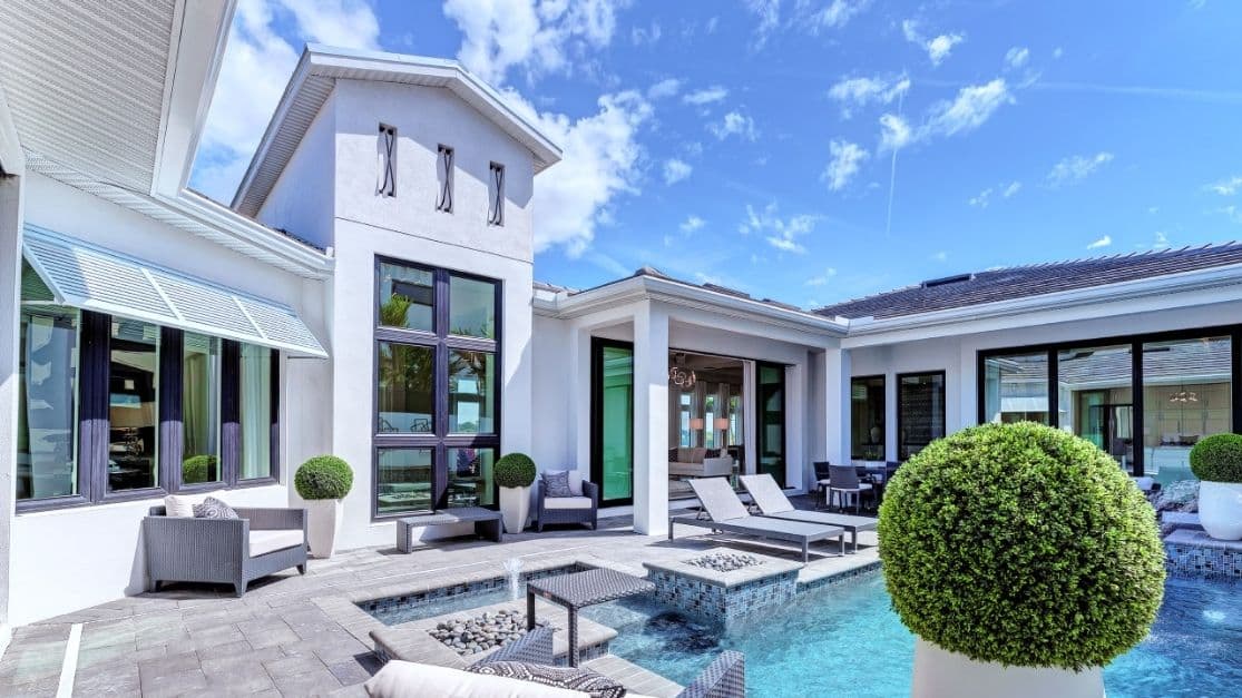 Modern white villa with a large glass doorway, pool, and outdoor lounge on a sunny day.