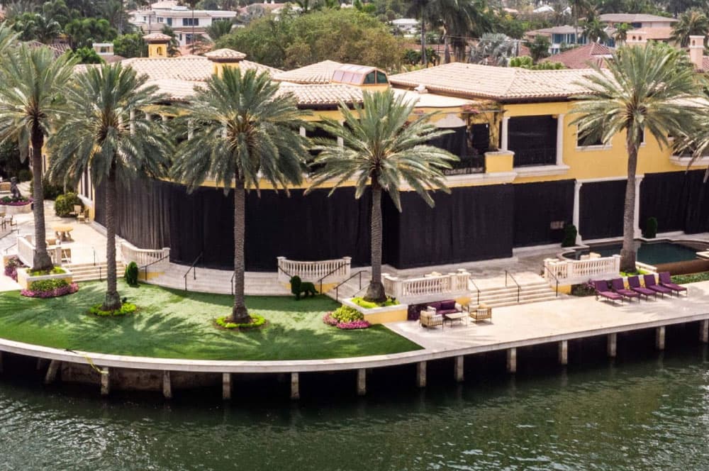 Waterfront home with yellow stucco exterior and black fabric hurricane shutters covering the windows.