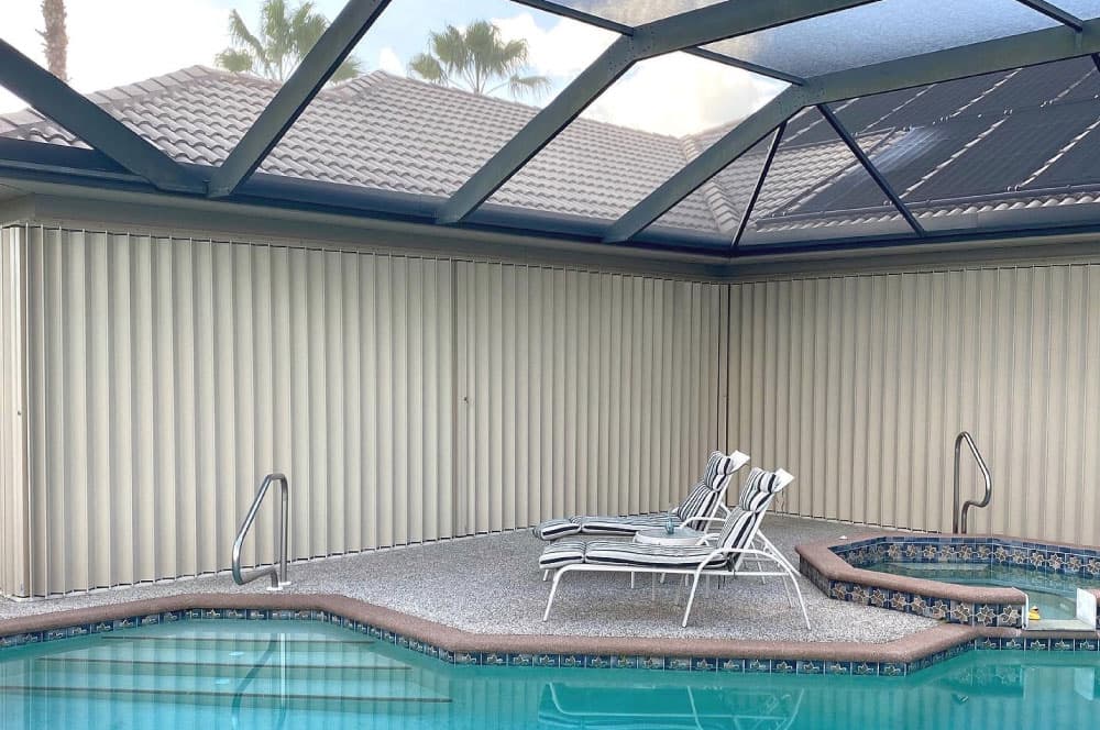 Enclosed pool area featuring accordion hurricane shutters, with lounge chairs on the patio