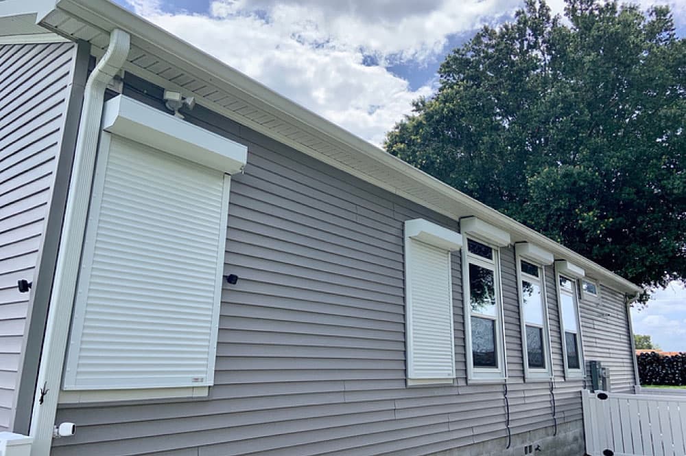 White roll-down hurricane shutters partially deployed over large windows.