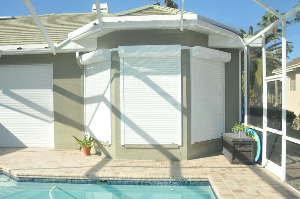 House with white roll-down hurricane shutters covering large windows