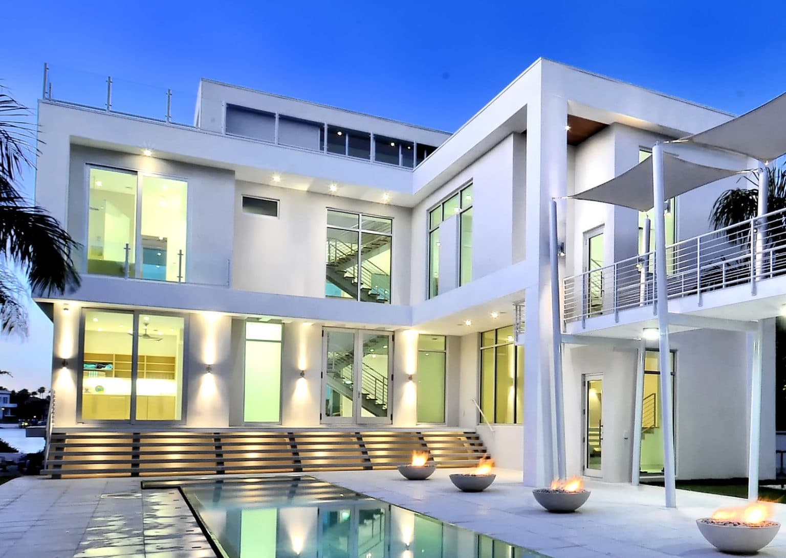 A modern white house with a swimming pool and outdoor fire pits.