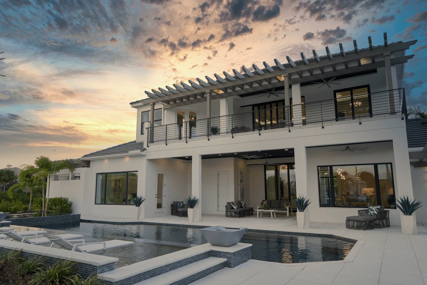 A modern white house with a pool and a pergola at sunset.