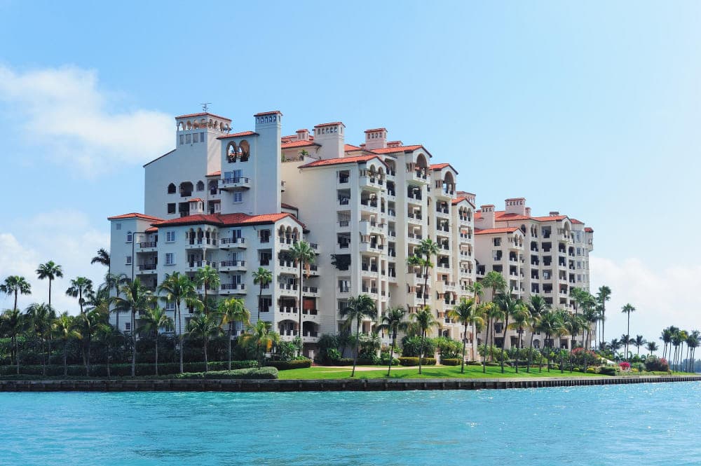 Waterfront condo building with palm trees and balconies under a clear blue sky.