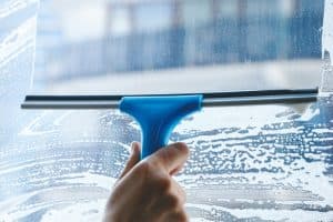 Hand using a squeegee to clean a soapy window.